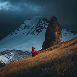 a woman in a red dress stands near a mountain under a dark sky