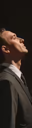 a male in a black jacket and tie and his eyes closed