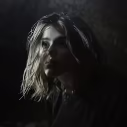 a woman with long hair and piercings stands in a dark room