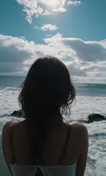 a woman standing on the beach looking at the water