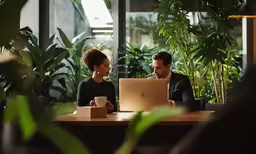 a man and woman sitting at a table using a laptop computer