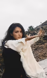 a woman posing on a hill while holding her arms in the air