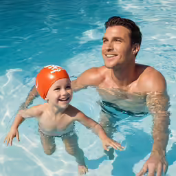 man and young boy with swimming cap in swimming pool