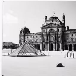 a black and white photo of a big building with a pyramid on the ground