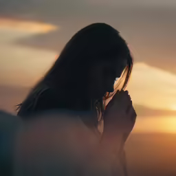 a woman praying in front of a sunset