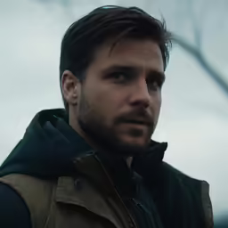 a close - up shot of a man standing outdoors with trees in the background