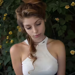 a woman that is standing by some flowers,a young lady standing in front of some flowers looking down at her cell phone