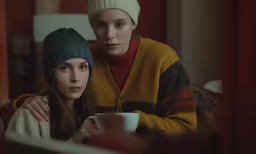 two young women are sitting together, holding cups