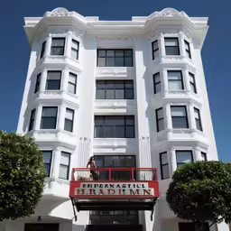 a woman in a red dress stands on the balcony of a white hotel