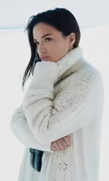 a woman standing outside wearing a white sweater and scarf