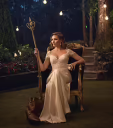 a woman wearing a gown and holding a staff is posing
