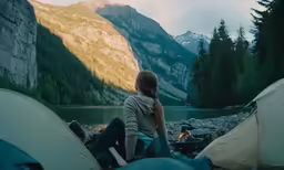 a woman sitting next to a tent in the mountains