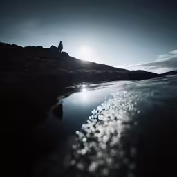a couple of people are sitting on a small hill above water