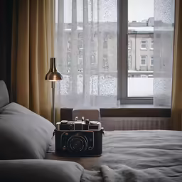 an antique camera sitting on a bed beside a window