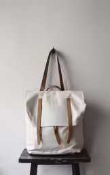 a white canvas bag with brown leather handles on a small table