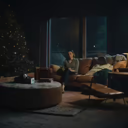 a woman sits on a couch watching a tv at christmas