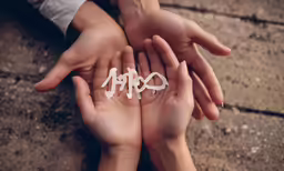 two hands holding up some paper letters on concrete