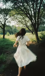 a woman walking down a dirt road near trees