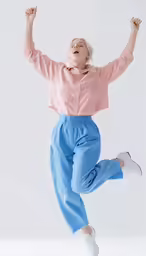 an excited woman jumps in the air wearing pants