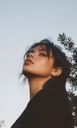 a woman is staring up at something with a tree in the background