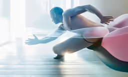 nude male model sitting on a pink chair with white ribbons across his body