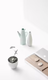 a table topped with computer, plant, and cell phone