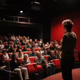 woman standing on stage looking at audience with red screen