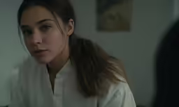 a woman with a ponytail wearing white shirt looking off into the distance