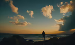 silhouette of a person standing on rock formation at sea