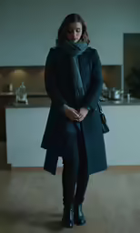 the woman in the long coat stands in front of a stove