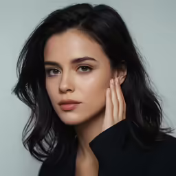 a woman with long black hair and hand on her ear