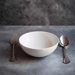 two spoons, one fork and a bowl are on the table