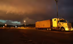 large semi - truck moving along a night roadway,a large truck parked on a road near a street lamp