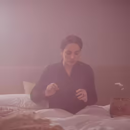 a woman looking at a bed with white sheets and an arrangement