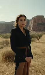 a woman in a suit in a field with a rock formation behind her