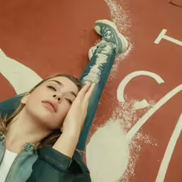 a girl sitting on the side of the road holding her hand up to her face