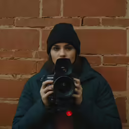 a woman with a camera up close and in front of a brick wall