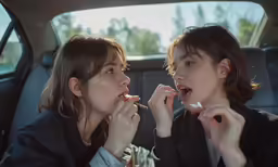 two young women sit in a car and smoke