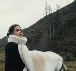 a woman standing with a white horse on a field