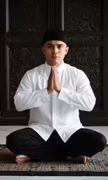 a man is in a white shirt and black pants sitting on a rug