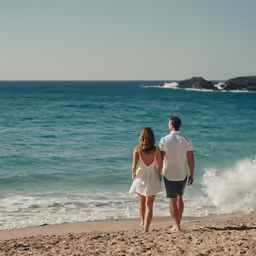 a man and a woman holding hands while walking along the beach