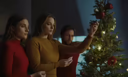 two women and man decorating a christmas tree
