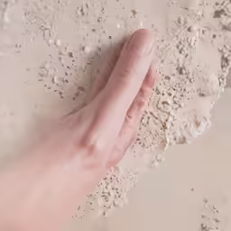 a hand with a nail on a sandy surface
