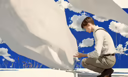 a woman leaning on a white structure with blue and white clouds