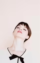 a woman with her eyes closed and her chin tucked in black on the neck, in profile, standing against a pink background