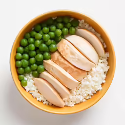 a yellow bowl with white rice, peas, chicken, and sliced meat