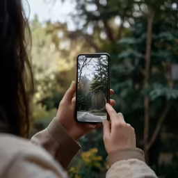 a person standing in a forest taking pictures on their phone