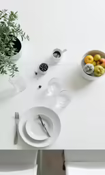 a white table with plates and cups and plants in them
