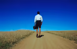 a man walking on dirt road with briefcase