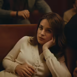 woman sitting with head in hands, dressed in elegant clothing